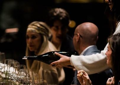 A sommelier pours wine for guests at a candlelit tasting dinner